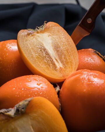 Fresh ripe persimmon fruit, winter fruit, cut on board and black backgroundの写真素材