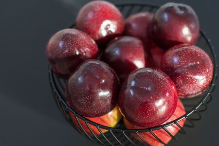 fresh round purple plums, in a black fruit bowl, on a black background. closelyの写真素材
