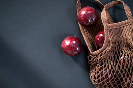 fresh round purple plums, in a string bag , cotton grocery bag on a black background.の写真素材