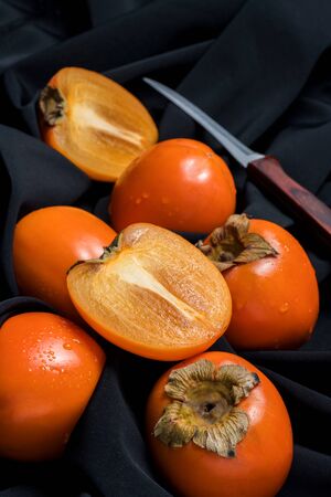 Fresh ripe persimmon fruit, winter fruit, cut on wooden board and black backgroundの写真素材