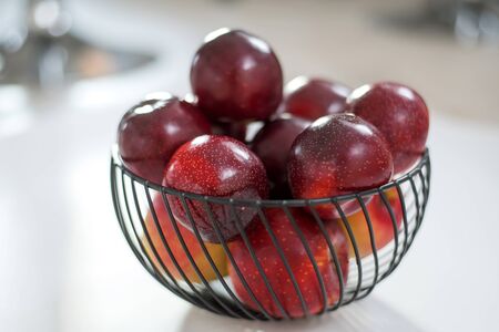 fresh round purple plums, in a black fruit bowl, on a grey background.の写真素材