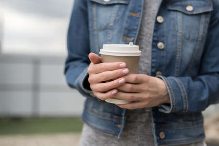 Womens hands in a denim jacket hold a Cup of coffee to go, zero westの写真素材
