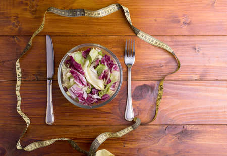 Fresh vegetable salad leaves in a glass bowl with a fork and knife, isolated on a wooden background close-upの写真素材