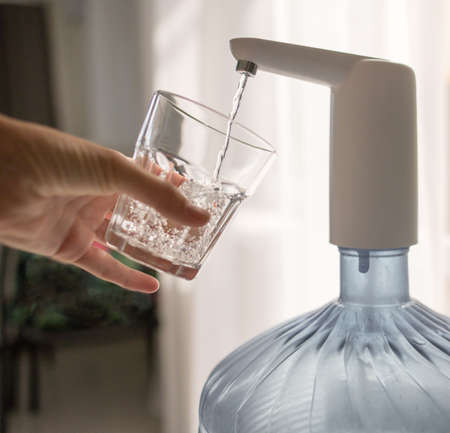 hand with a glass pours water from the coolerの写真素材