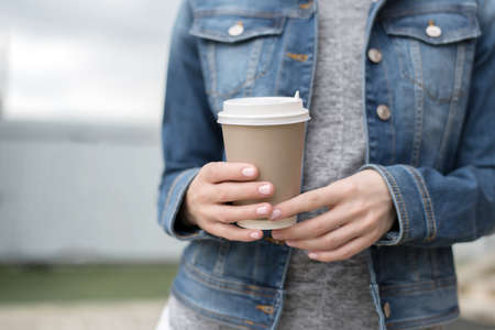 Womens hands with pink manicure in a denim jacket hold a Cup of coffee to go, zero westの写真素材