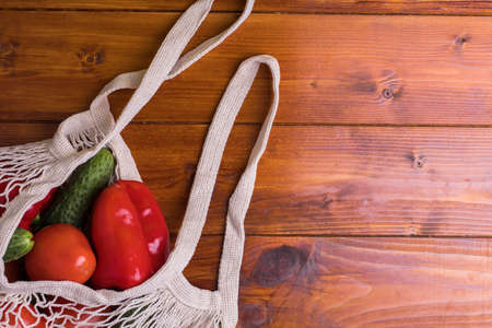 Eco bag string bag with vegetables cucumbers and tomatoes on a wooden background. Zero Westの写真素材