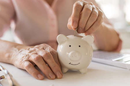 Old women's hands put money in the piggy Bank, the concept of retirement, savings.の写真素材