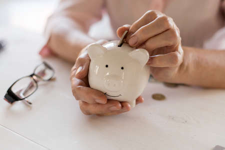 Old womens hands put money coins in a piggy Bank, the concept of retirement, savings, savings, old age.の写真素材