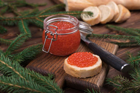 Red caviar in a glass jar on a brown wooden background with a Christmas tree. The main dish of the New year.の写真素材