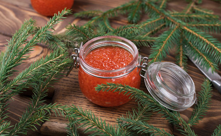 Red caviar in a glass jar on a seasoned white wooden background with a Christmas tree. The main dish of the New yearの写真素材