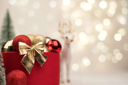 Red Christmas gift box with a gold bow on the background of bokeh, Christmas trees and toys.の写真素材
