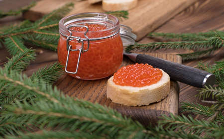 Red caviar in a glass jar on a brown wooden background with a Christmas tree. The main dish of the New yearの写真素材