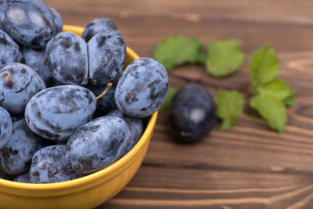 Lots of ripe juicy plums in a orange bowl on the wooden tableの写真素材