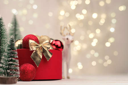 Red Christmas gift box with a gold bow on the background of bokeh, Christmas trees and toys.の写真素材