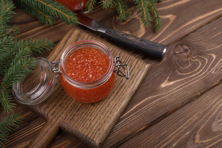 Red caviar in a glass jar on a seasoned white wooden background with a Christmas tree.の写真素材
