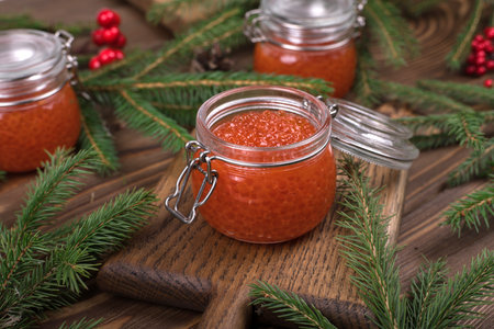 Red caviar in a glass jar on a seasoned white wooden background with a Christmas tree.の写真素材