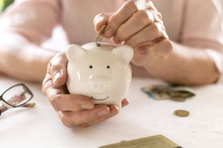 Old women's hands put money in the piggy Bank, the concept of retirement, savings.の写真素材