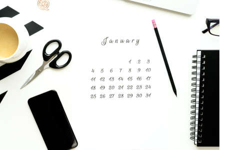 Calendar of January on white desktop flat ley with a cup of coffee and a notebook.の写真素材