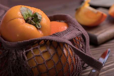 Ripe orange persimmon fruit.Close-up of fresh persimmons in a string bag on a wooden background. Zero West.の写真素材