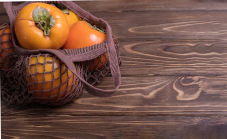 Ripe orange persimmon fruit.Close-up of fresh persimmons in a string bag on a wooden background. Zero West.の写真素材
