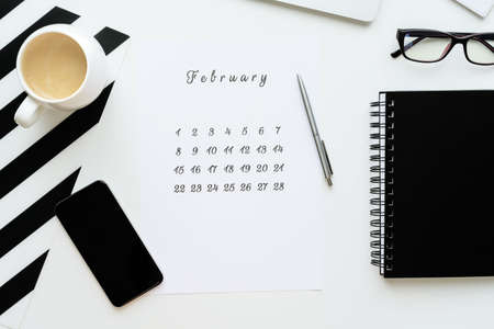 Calendar of February on white desktop flat ley with a cup of coffee and a notebook.の写真素材