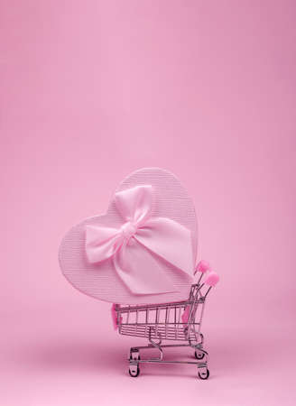 Pink big heart-shaped gift with bow for Valentine's Day in shopping scart on a pink background, minimalism.の写真素材