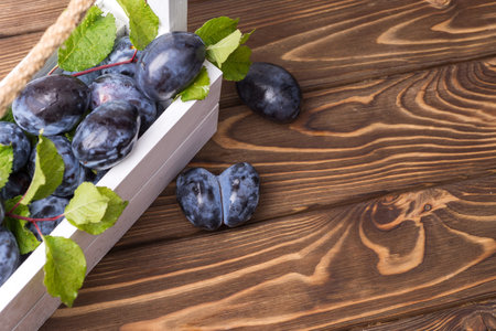 Lots of ripe juicy plums in a white box on the wooden table