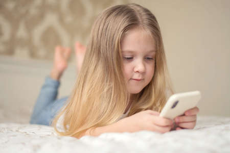 Little girl in bed playing a tablet in social internet. Close up of little girl watching video on the digital tabletの写真素材