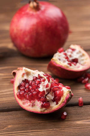 Fresh, ripe, juicy pomegranate fruit is divided into pieces on a brown wooden background.の写真素材