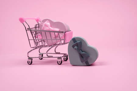 Pink big heart-shaped gift with bow for Valentine's Day in shopping scart on a pink background, minimalism.の写真素材
