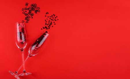 Two glasses of champagne filled with heart shaped sequins on a red background valentine's day.の写真素材