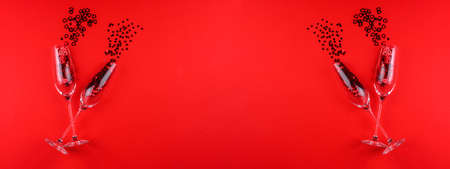 Two glasses of champagne filled with heart shaped sequins on a red background valentine's day.の写真素材