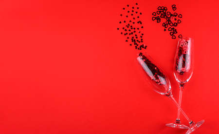 Two glasses of champagne filled with heart shaped sequins on a red background valentine's day.の写真素材