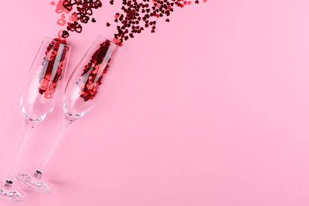 Two glasses of champagne filled with heart shaped sequins on a pink background valentine's day.の写真素材
