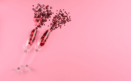 Two glasses of champagne filled with heart shaped sequins on a pink background valentine's day.