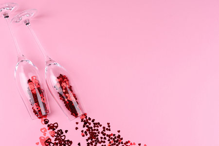 Two glasses of champagne filled with heart shaped sequins on a pink background valentine's day.の写真素材