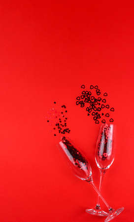 Two glasses of champagne filled with heart shaped sequins on a red background valentine's day.の写真素材