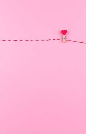 Tender little heart symbol of St. Valentine's day on a clothespin and string creative postcard, copy space, flat lay on pink backgroundの写真素材