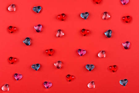 A scattering of colored glass hearts on red background for Valentine's Dayの写真素材