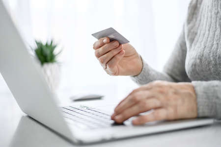 Hands of a woman senior work at a laptop with credit card using modern technology in everyday life. online shoppingの写真素材