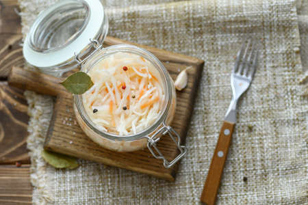 Sour, pickled sauerkraut with carrots and bay leaves in a glass jar.の写真素材