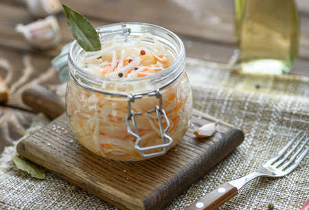 Sour, pickled sauerkraut with carrots and bay leaves in a glass jar.の写真素材