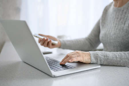Hands of a woman senior work at a laptop with phone using modern technology in everyday life. online shoppingの写真素材