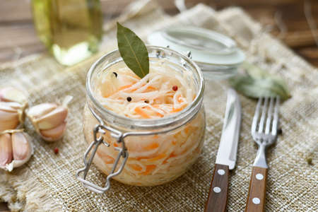 Sour, pickled sauerkraut with carrots and bay leaves in a glass jarの写真素材