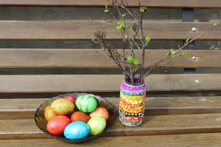 photo on a wooden bench, colored Easter eggs and jar with branches