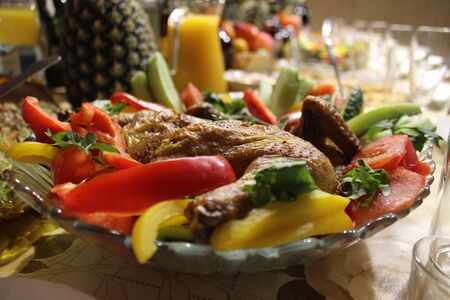 a close-up photo of a plate with a baked chicken and fresh vegetables on a festive tableの写真素材