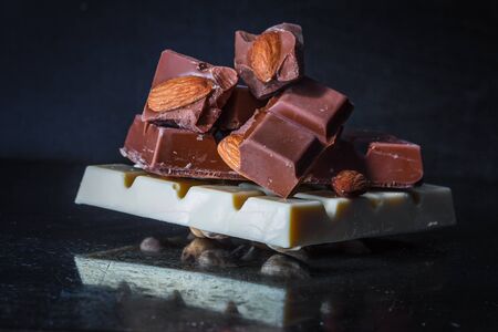 Slices of milk chocolate with almonds and tiles of white chocolate with hazelnuts on an old dark metallic backgroundの写真素材