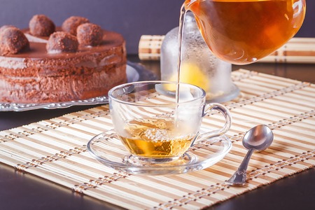 Pouring tea from a transparent glass teapot into a clear glass cup on a saucerの写真素材