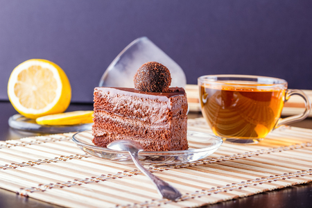 A piece of homemade chocolate biscuit cake on a transparent glass plate, a spoon and a cup of teaの写真素材