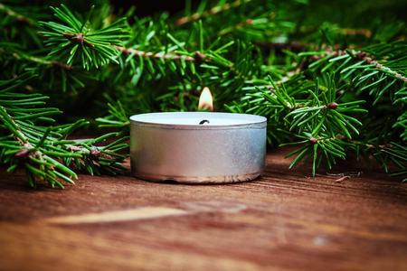A burning candle and spruce branches on a wooden table. Selective focus. Copy space. Christmas, New Year backgroundの写真素材